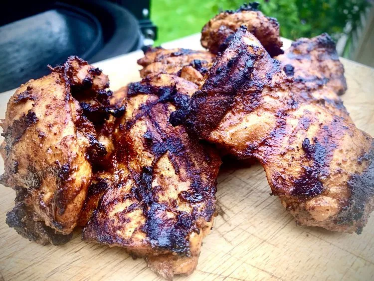 Charred chicken thighs resting on a wooden board