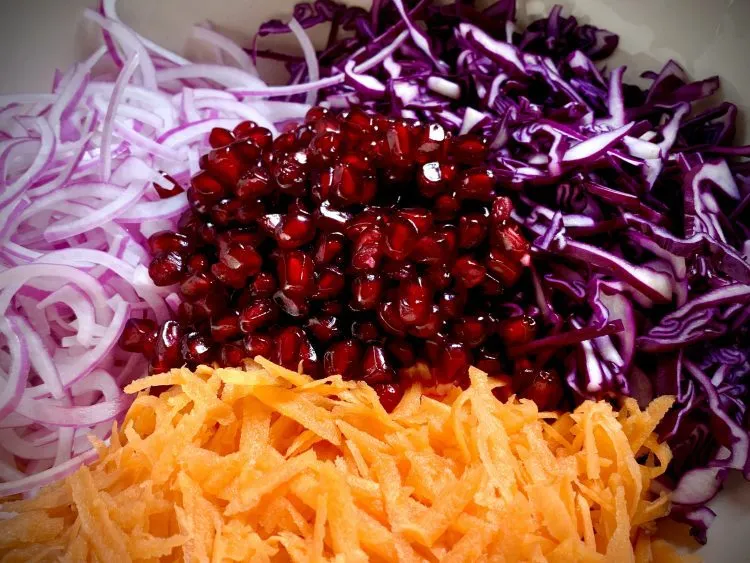 Red cabbage, grated carrot, red onion and pomegranate seeds in a mixing bowl, before mixing