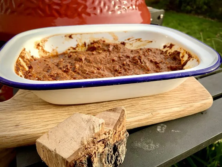Marinated skirt steak in an enamel dish beside a chunk of hickory wood, in front of the kamado