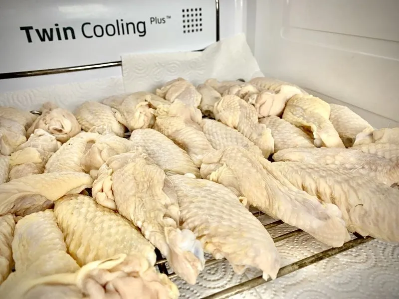 Brined chicken wings on a rack over kitchen roll in the fridge