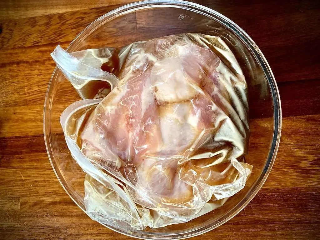 Pork sealed in a bag of brine, sitting in a glass bowl